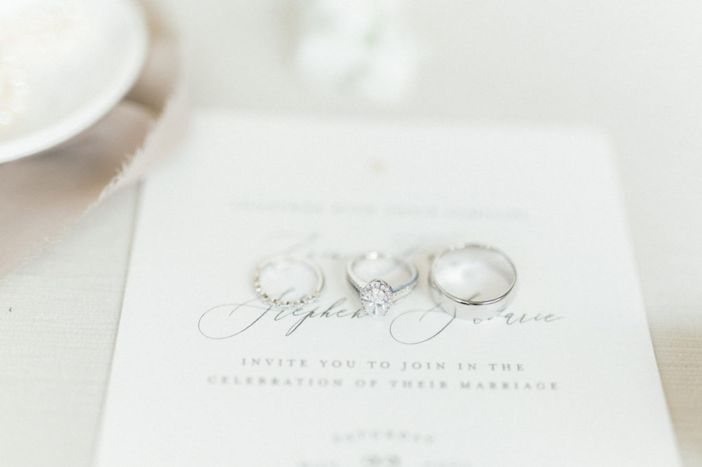 A detail shot of Erin and Stephen's wedding rings placed on top of one of their wedding invitations. Erin's oval engagement ring is in the center. 