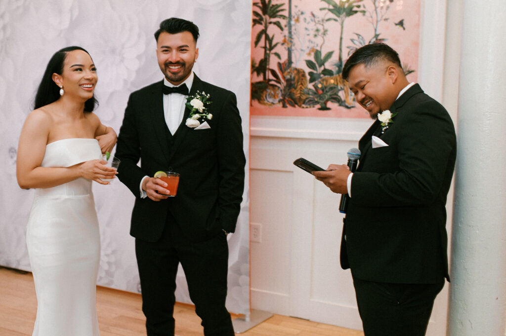 Bride, groom, and groomsman laughing during heartfelt reception toasts at Common House Richmond, photographed by Virginia wedding photographer Chelsea Schmidt.