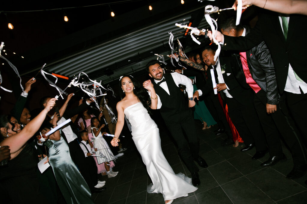 Bride and groom running through a ribbon exit surrounded by cheering guests during their Common House Richmond wedding, photographed by Chelsea Schmidt Photography.