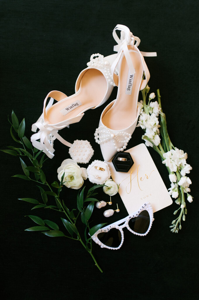 flat lay shot of bridal details like shoes, ring, and sunglasses.